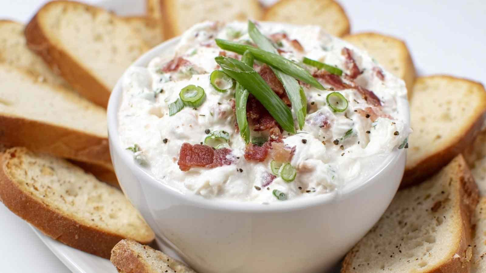 Close-up of bagel dip topped with bacon and scallions, surrounded by toasted bagel chips.