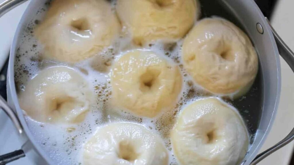 Sourdough discard bagels boiling in a pot of water with foam on the surface.
