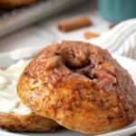 Close-up of a cinnamon crunch bagel sliced and served with a thick layer of whipped cream cheese on a white plate.