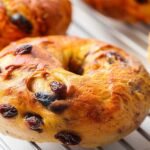 Close-up of a golden-baked cinnamon raisin bagel on a cooling rack, highlighting the glossy crust and visible raisins