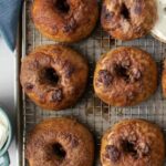 Overhead shot of several cinnamon crunch bagels on a cooling rack, golden and caramelized, with cream cheese on the side.