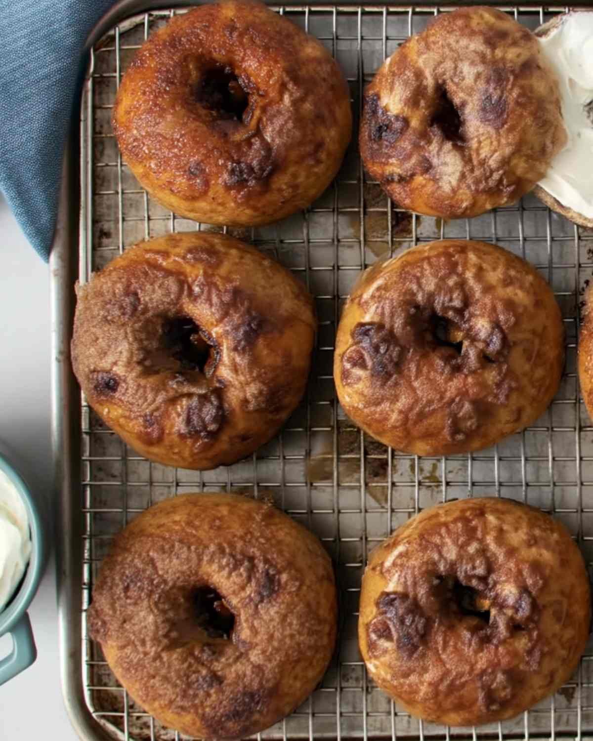 Overhead shot of several cinnamon crunch bagels on a cooling rack, golden and caramelized, with cream cheese on the side.