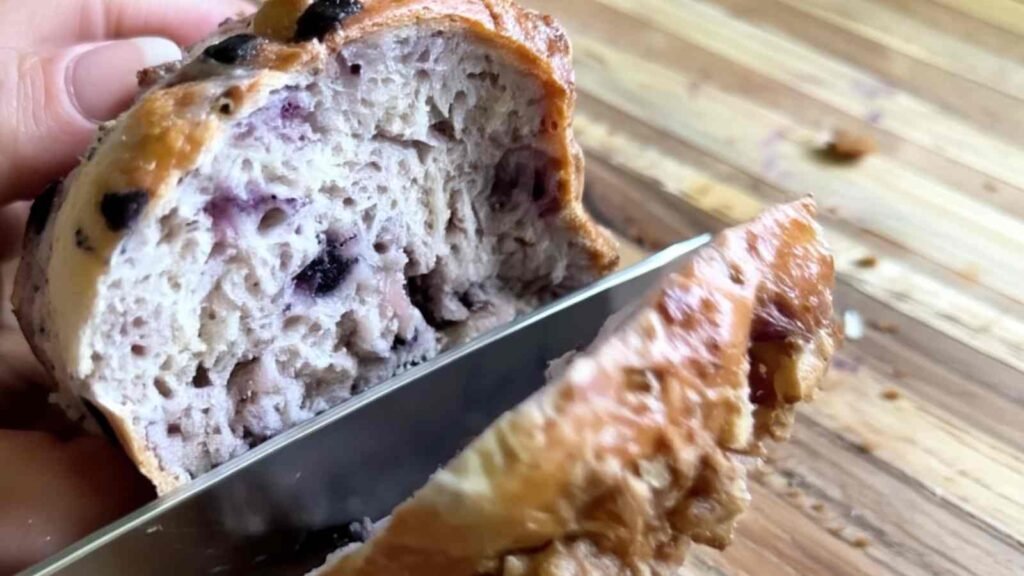 Slicing into a freshly baked blueberry bagel with a knife, showing its airy crumb and golden crust.