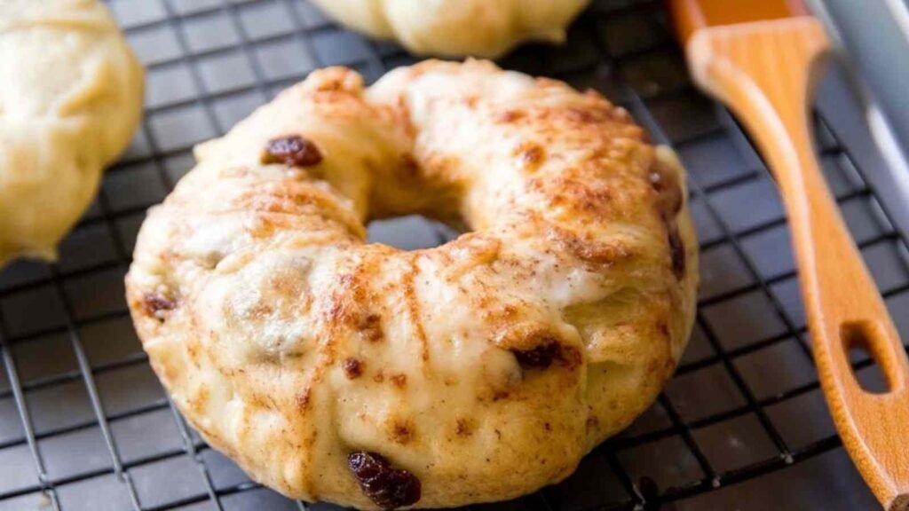 Egg-washed cinnamon raisin bagel resting on a cooling rack, with a shiny and golden exterior
