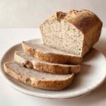 Finished flourless bread loaf on plate, partially sliced to show inside crumb and crust