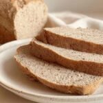 Close-up of sliced flourless bread on a ceramic plate showing its soft, dense interior and golden crust