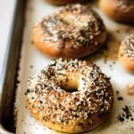Freshly baked everything bagels with golden crusts on a baking tray lined with parchment