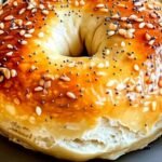 Close-up of a golden-brown Greek yogurt bagel with a glossy egg wash and everything bagel seasoning, baked to perfection