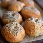 Baked sourdough discard bagels arranged on a rustic wooden tray with parchment paper.