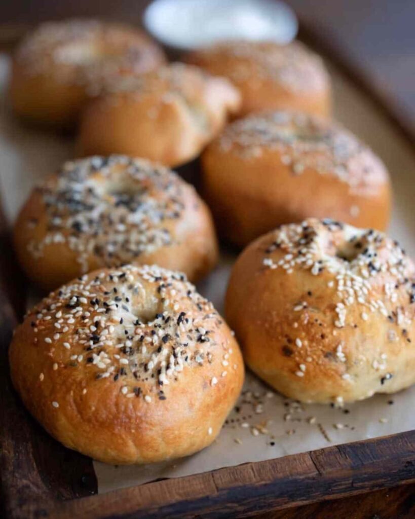 Baked sourdough discard bagels arranged on a rustic wooden tray with parchment paper.