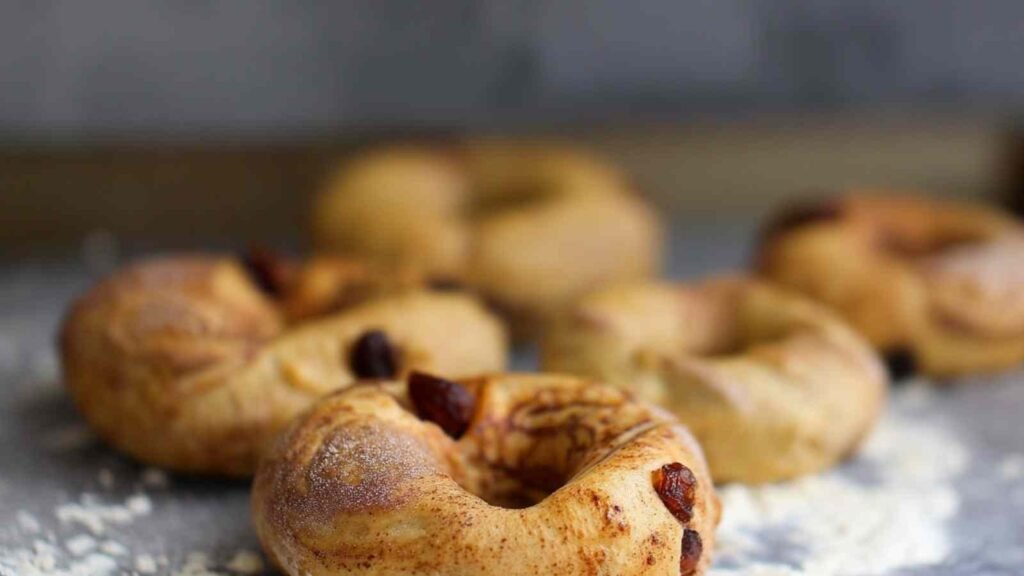 Unbaked cinnamon raisin bagels dusted with flour, laid out on a baking surface

