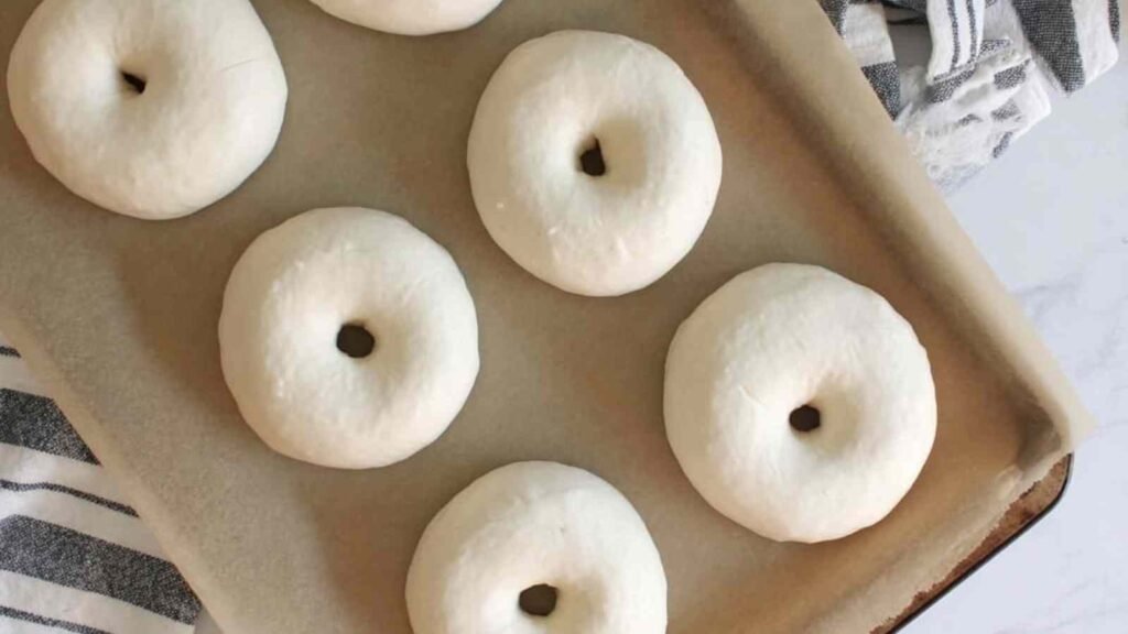 Tray of raw, shaped sourdough discard bagels resting before boiling.
