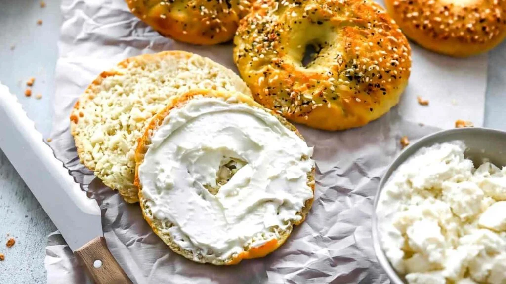 Sliced Cottage Cheese Bagel with Almond Flour spread with cream cheese on parchment with more bagels in background