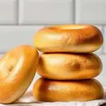 A vertical stack of five golden Hero Bagels on a white towel, set against a subway tile background.