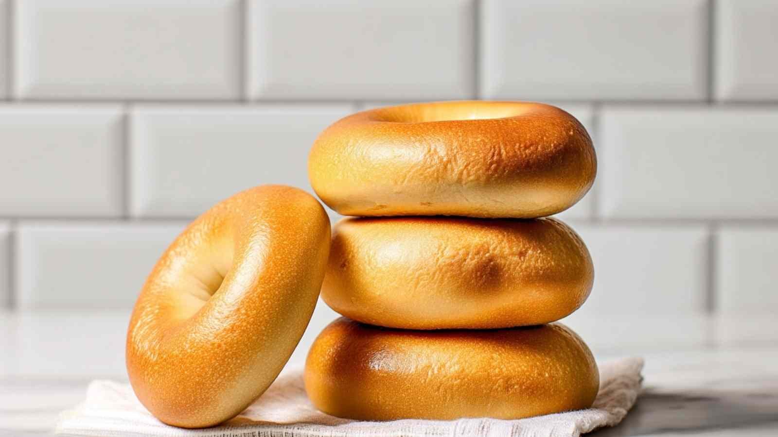A vertical stack of five golden Hero Bagels on a white towel, set against a subway tile background.