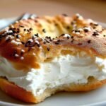 Close-up of a basket lined with parchment, filled with golden brown cottage cheese bagels topped with everything seasoning.