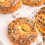 Five golden brown cottage cheese bagels topped with everything seasoning on a parchment-lined baking tray