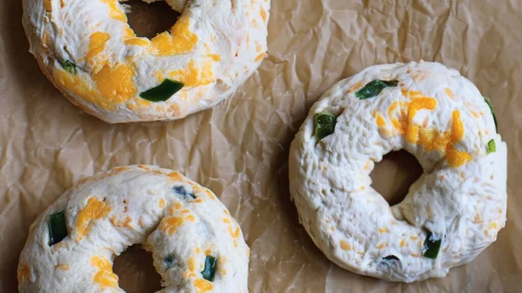 Unbaked jalapeno cheddar bagels arranged on parchment paper, showing visible jalapeño and cheddar bits in the dough.