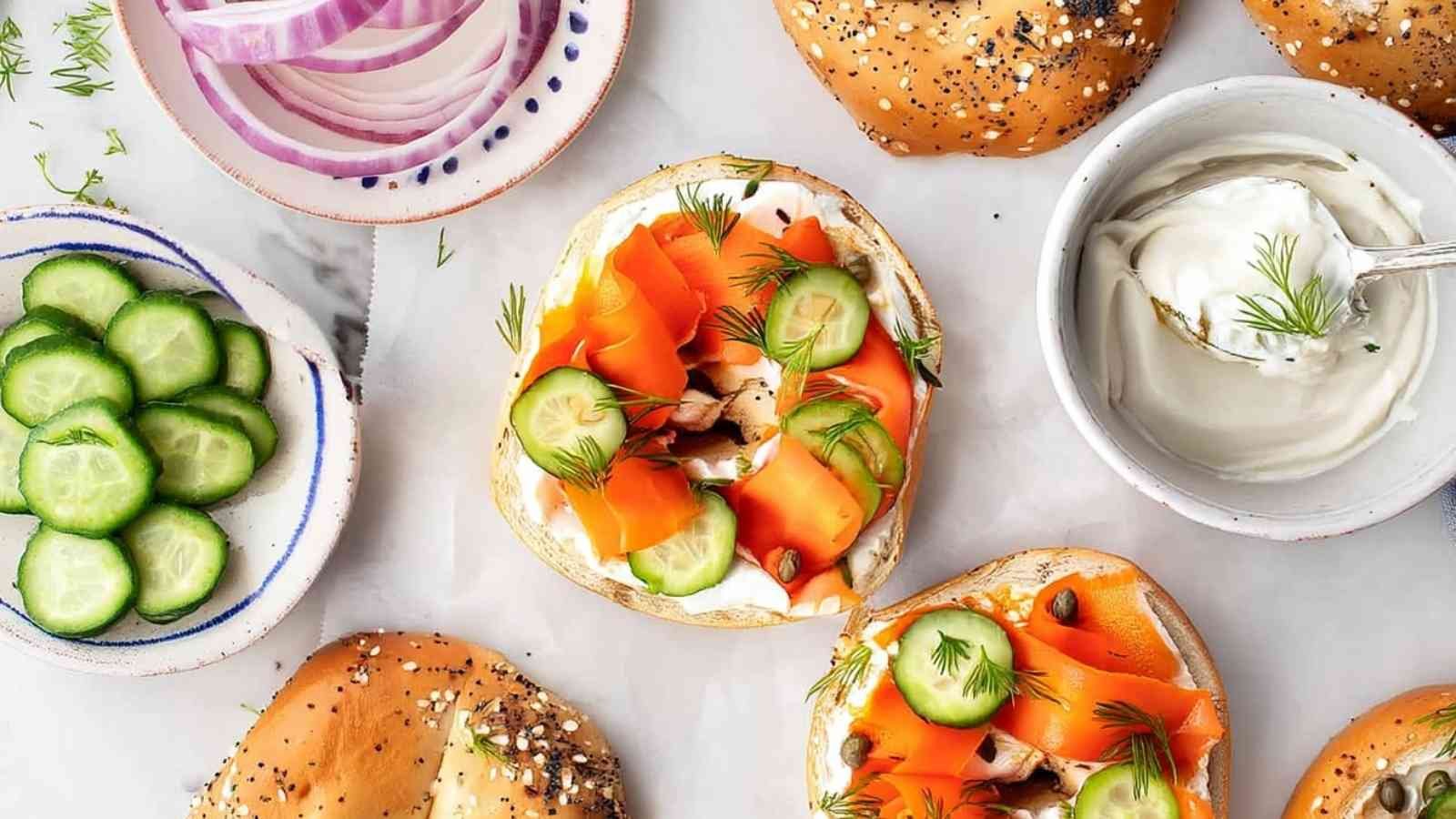 Flat lay of vegan lox bagels with sliced cucumbers, red onions, dill, and cream cheese in small bowls.