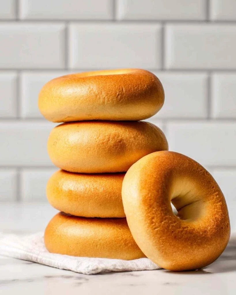 Tall stack of five plain Hero Bagels in vertical orientation on white towel with tile backdrop.