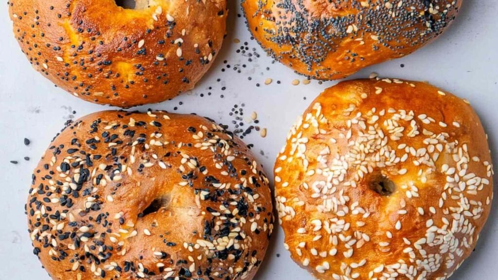 Close-up of four air-fried cottage cheese bagels topped with sesame seeds, poppy seeds, and everything seasoning on a white surface.