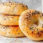 Close-up of stacked golden high protein bagels topped with everything bagel seasoning, resting on a marble board.