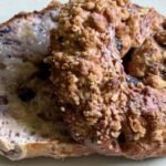 Close-up of a sliced Greek yogurt blueberry bagel, one half topped with cinnamon-sugar crumble and the other revealing a moist, blueberry-speckled interior.