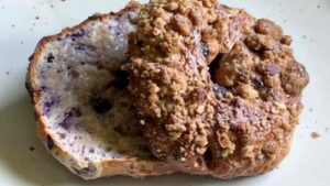Close-up of a sliced Greek yogurt blueberry bagel, one half topped with cinnamon-sugar crumble and the other revealing a moist, blueberry-speckled interior.