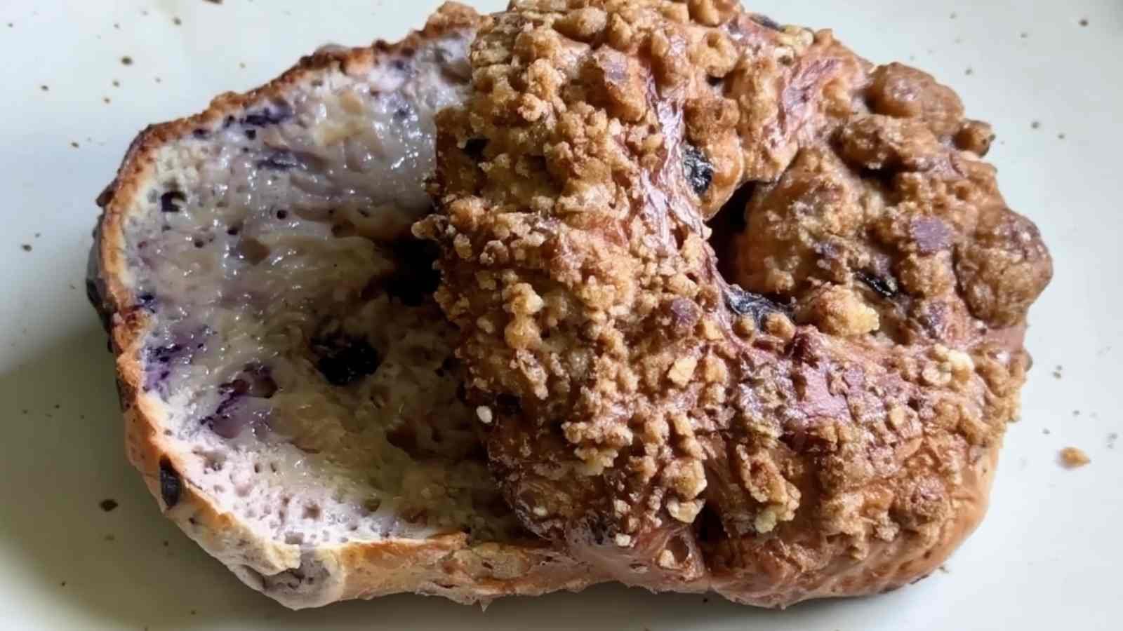 Close-up of a sliced Greek yogurt blueberry bagel, one half topped with cinnamon-sugar crumble and the other revealing a moist, blueberry-speckled interior.