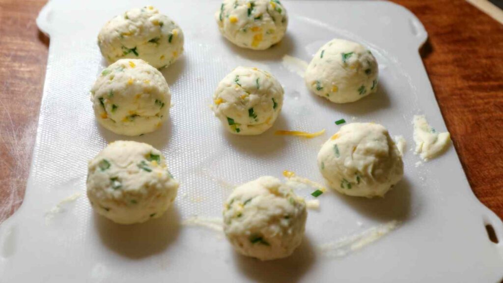 Small dough balls mixed with cheddar and jalapeño resting on a white cutting board before shaping into bagels