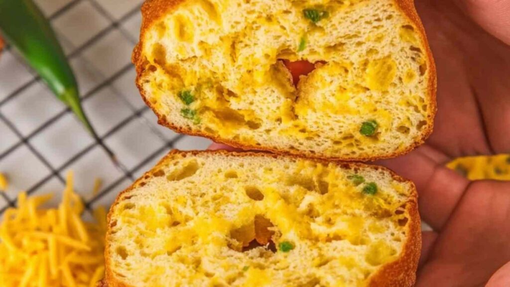 Close-up view of a sliced gluten-free jalapeño cheddar bagel, showing a fluffy interior with pockets of melted cheese and green jalapeño bits