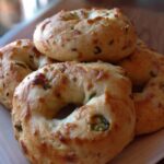Stack of freshly baked spicy jalapeño bagels on a white ceramic plate near a sunny window, with visible bits of chili and jalapeño
