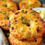 Tall stack of golden jalapeño cheddar protein bagels with blistered cheese tops and green chili slices