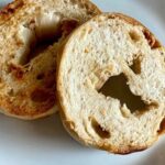 Two golden brown toasted bagel halves placed on a white plate, showing a crisp crust and airy interior