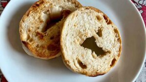 Two golden brown toasted bagel halves placed on a white plate, showing a crisp crust and airy interior