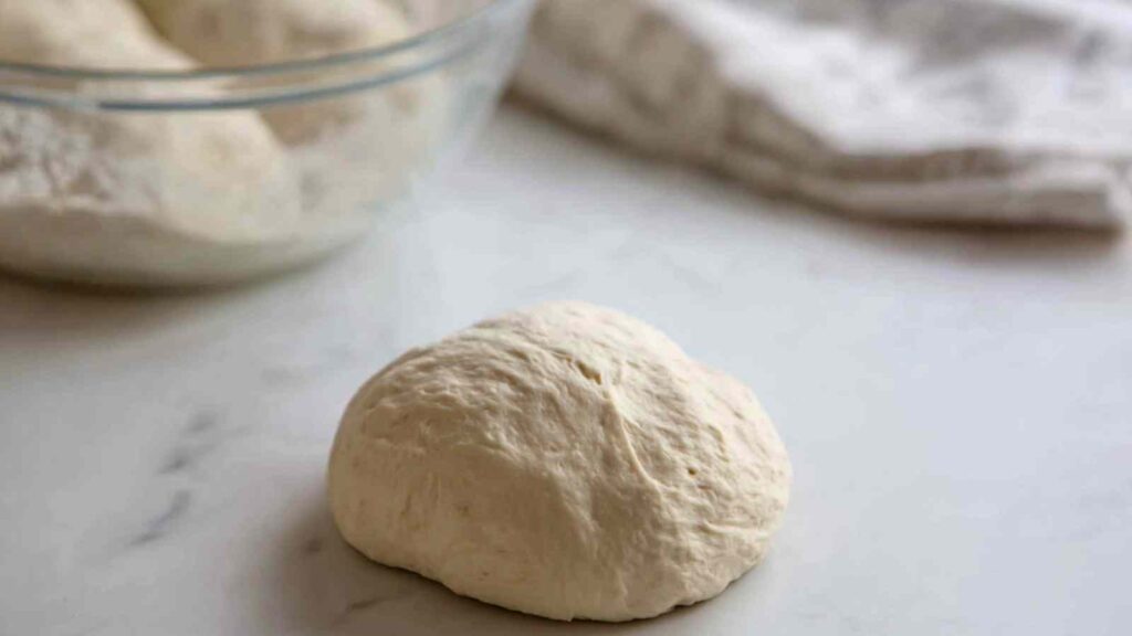 A single smooth dough ball placed on a floured surface before shaping