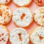 Top-down image of bagels spread with various cream cheese blends and garnished with herbs.