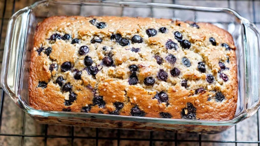 Freshly baked blueberry oat bread in a glass loaf pan, golden brown and dotted with blueberries