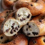 Golden baked chocolate chip bagels, close up with cream cheese filling visible inside.