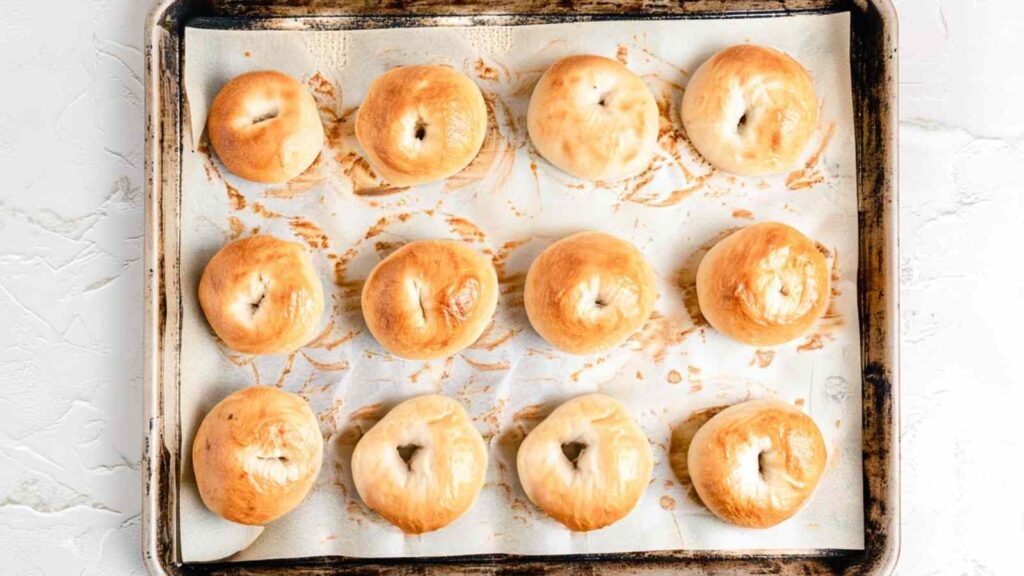 Freshly baked golden brown mini bagels on a parchment-lined baking sheet, just out of the oven.