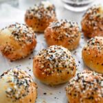 Overhead view of baked everything bagel bites on parchment, with seasoning scattered around