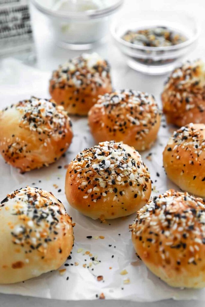 Overhead view of baked everything bagel bites on parchment, with seasoning scattered around