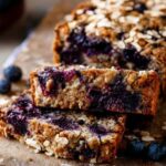 Close-up of blueberry oat bread slice with visible berries and oat flakes, set on a rustic board