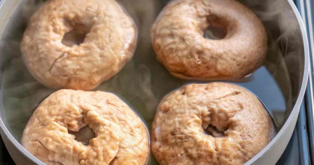 Four bagels boiling in a pot of water before baking, part of the Thomas' high protein bagel cooking process