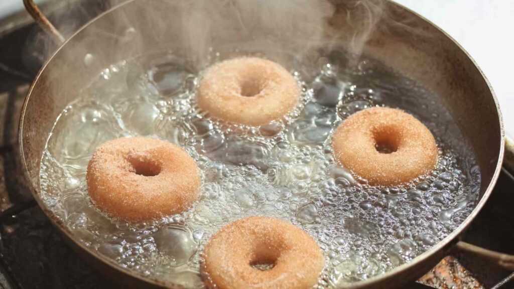 Whole wheat bagels simmering in a pan of water on the stovetop, steam rising