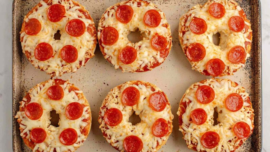 Bagel halves topped with mozzarella and pepperoni, placed on a baking tray before air frying.