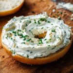 Toasted bagel half generously spread with homemade chive cream cheese and topped with chives and sesame seeds