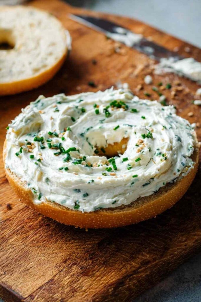 Toasted bagel half generously spread with homemade chive cream cheese and topped with chives and sesame seeds