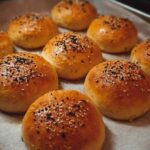 Baked bagel minis on a tray with parchment, golden brown with a shiny finish and seeded topping