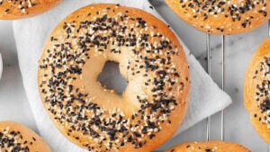 Close-up of a golden-brown sesame bagel topped with black and white sesame seeds resting on a cooling rack with a white towel underneath